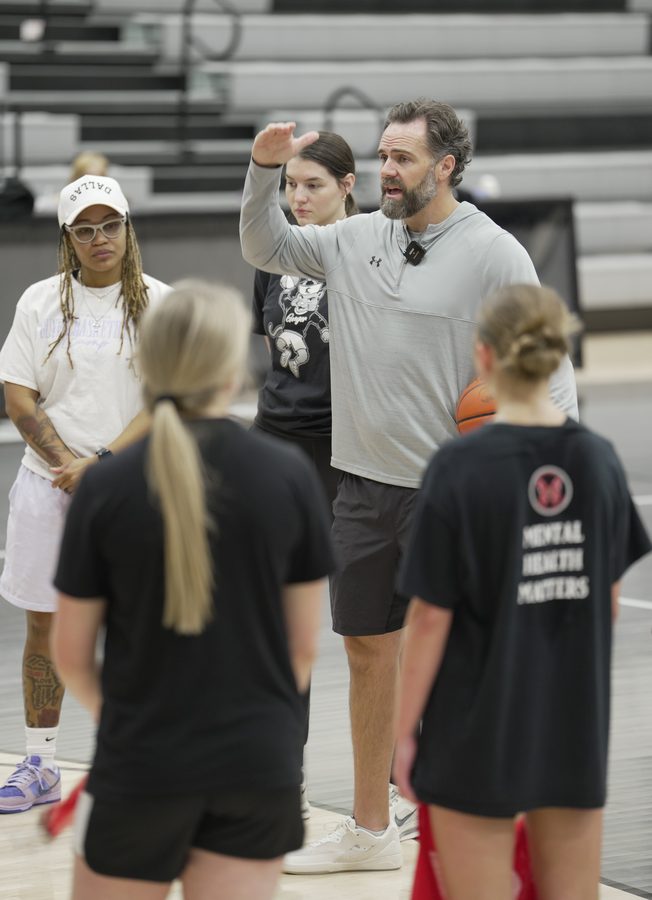 Coach Floyd demonstrates with a raised hand while players and coaches look on.